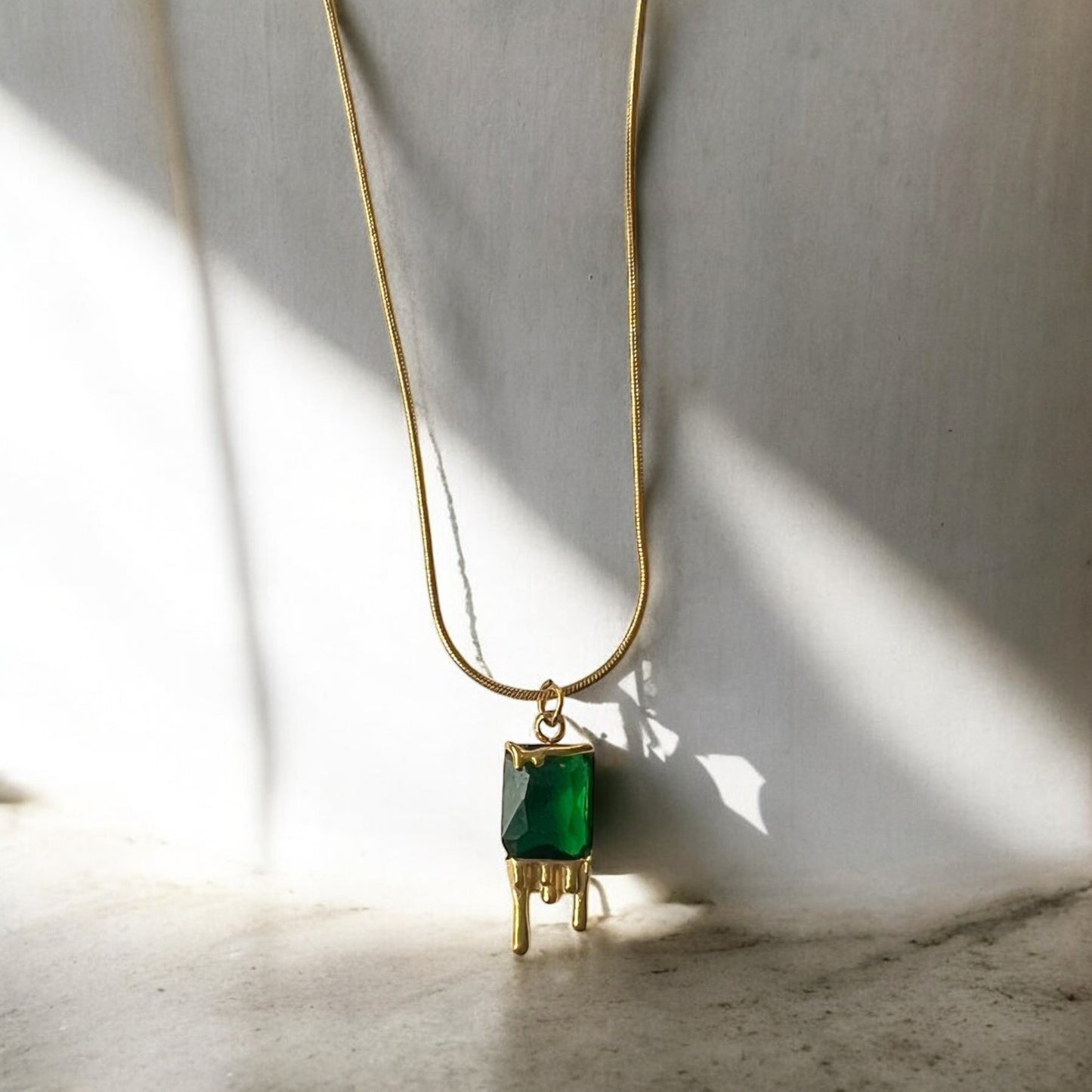 Gold necklace with a green pendant on a light background