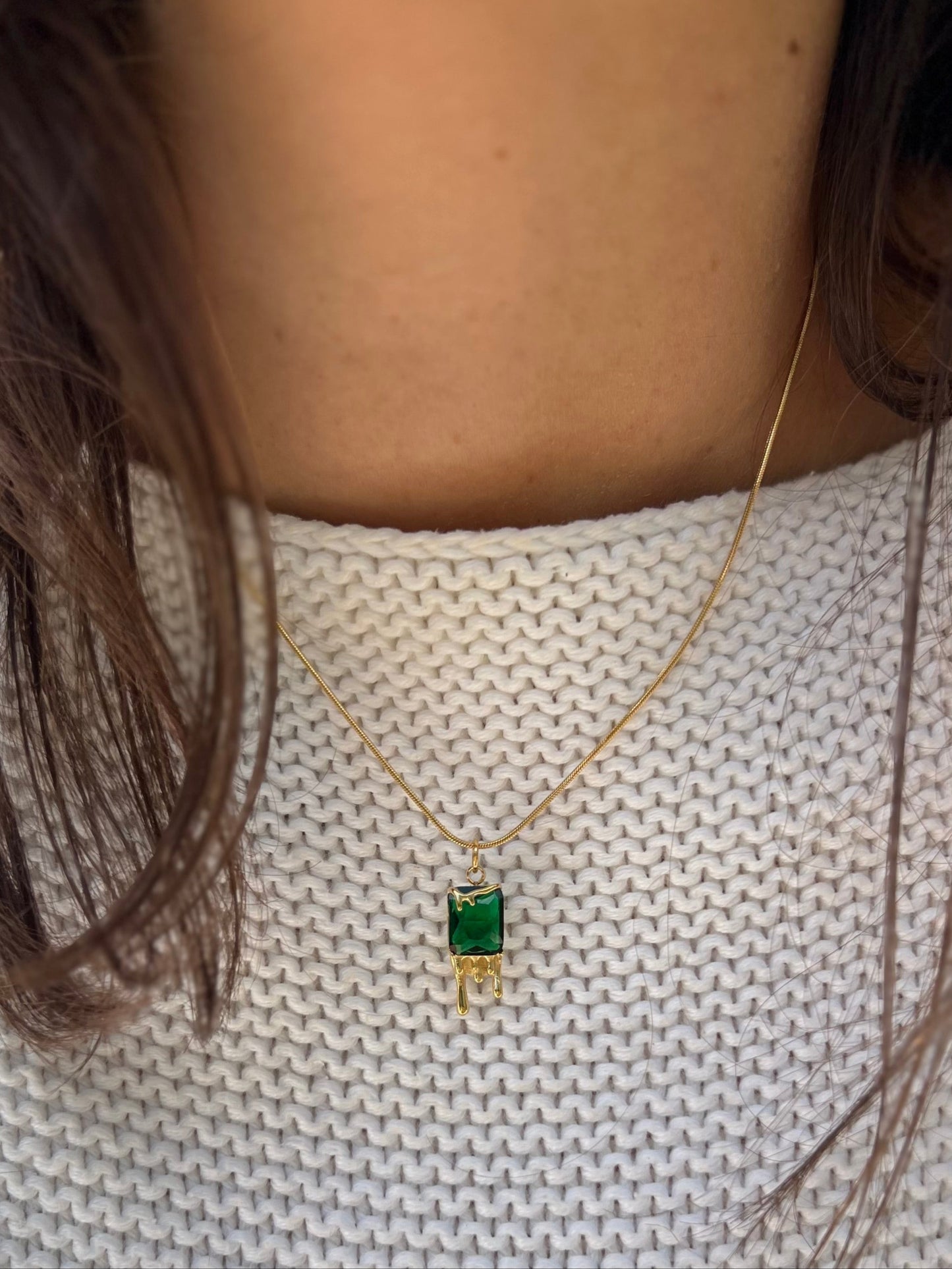 Necklace with a green gemstone pendant worn by a person on a light gray background