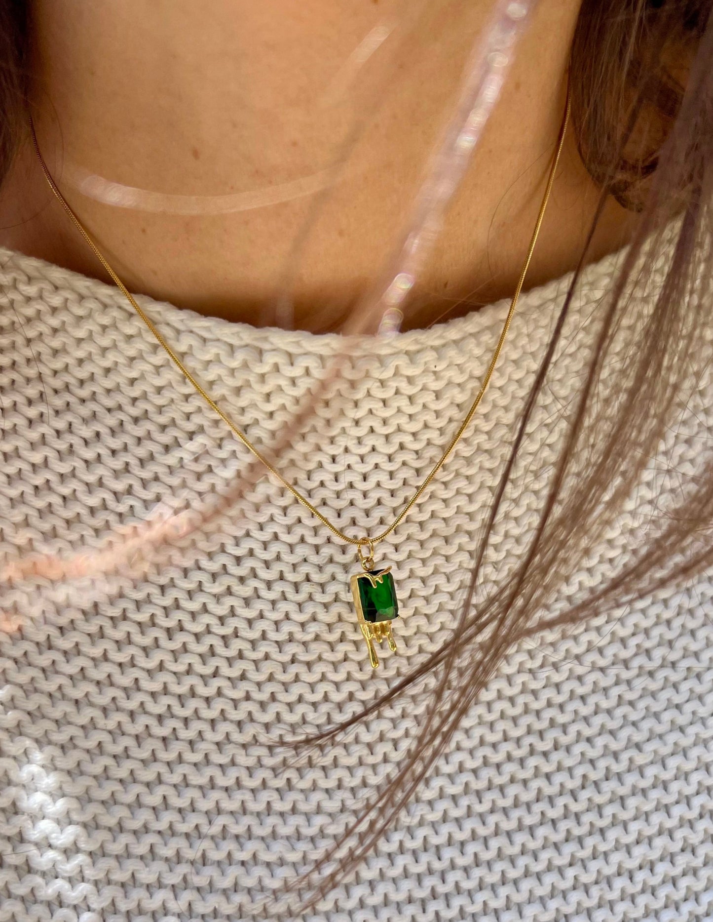 Close-up of a gold necklace with a green gemstone pendant on a textured beige background.
