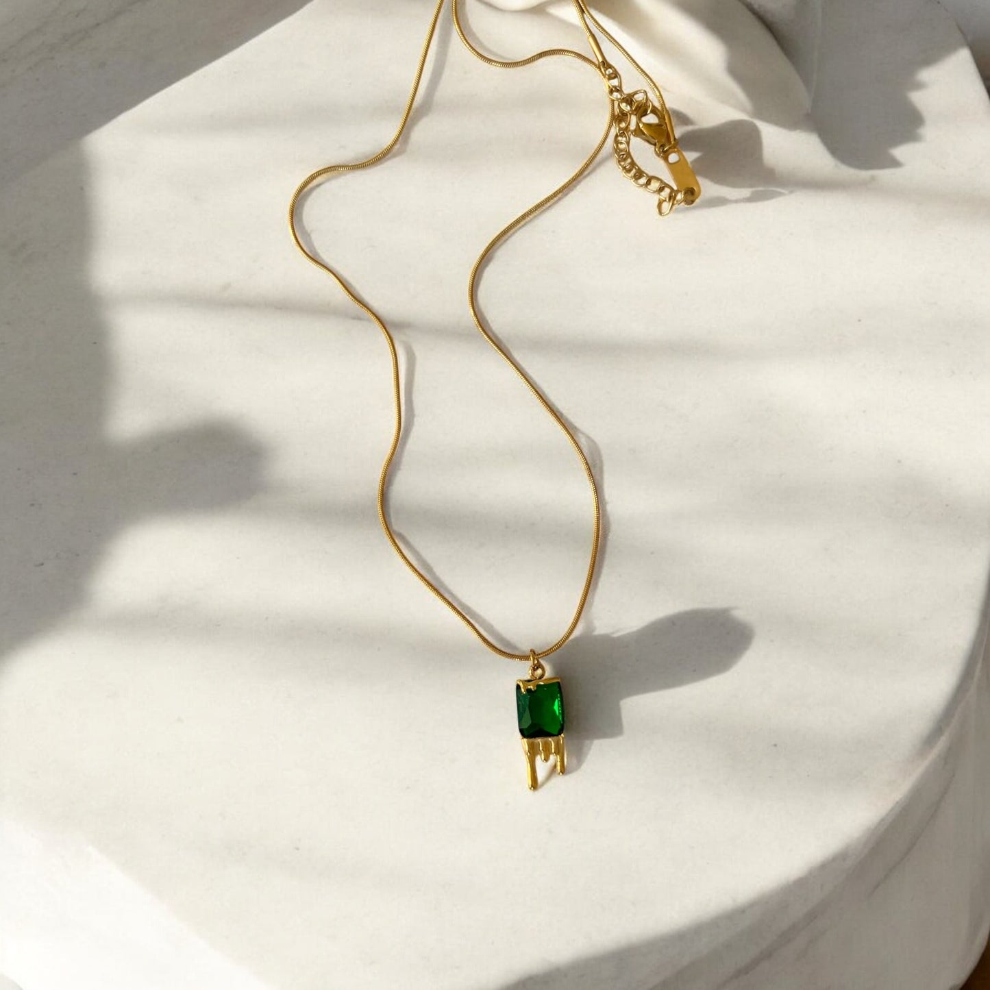 Gold necklace with a green gemstone pendant on a light background
