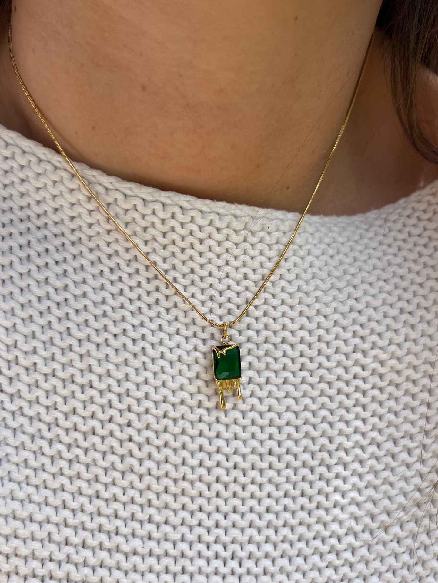 Gold necklace with a green gemstone pendant on a textured white fabric background