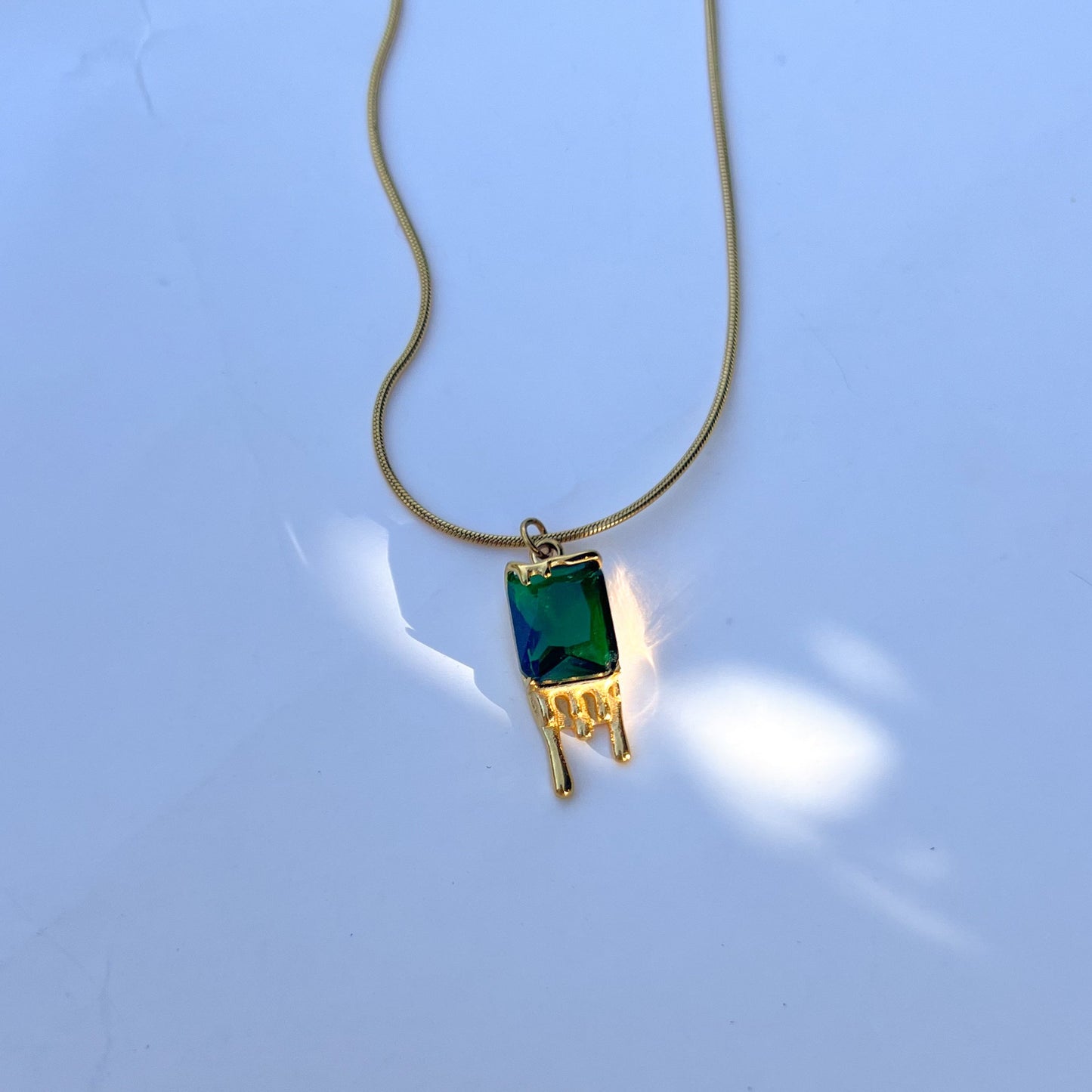 Gold necklace with a green gemstone pendant on a light blue background