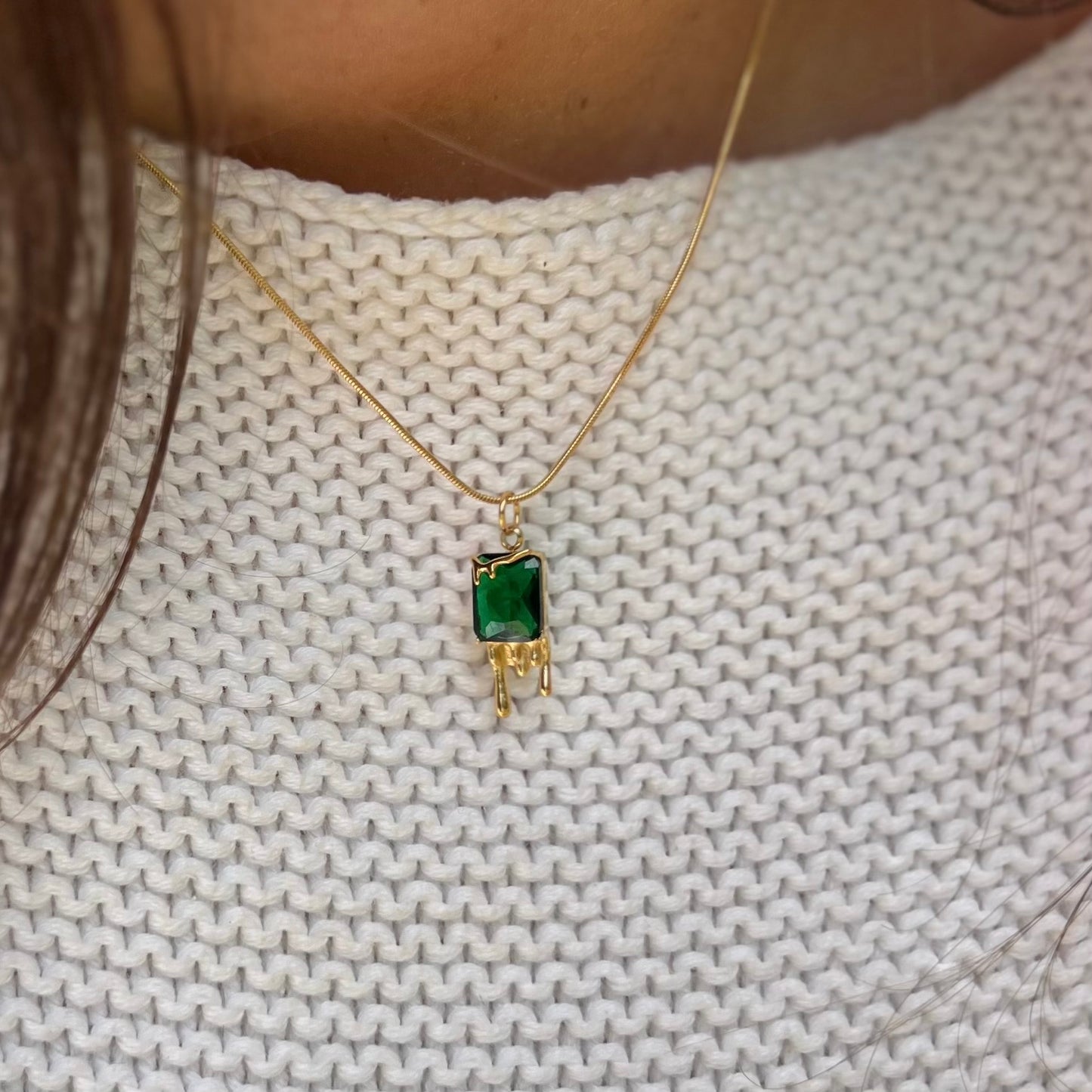 Gold necklace with a green pendant on a textured white fabric background