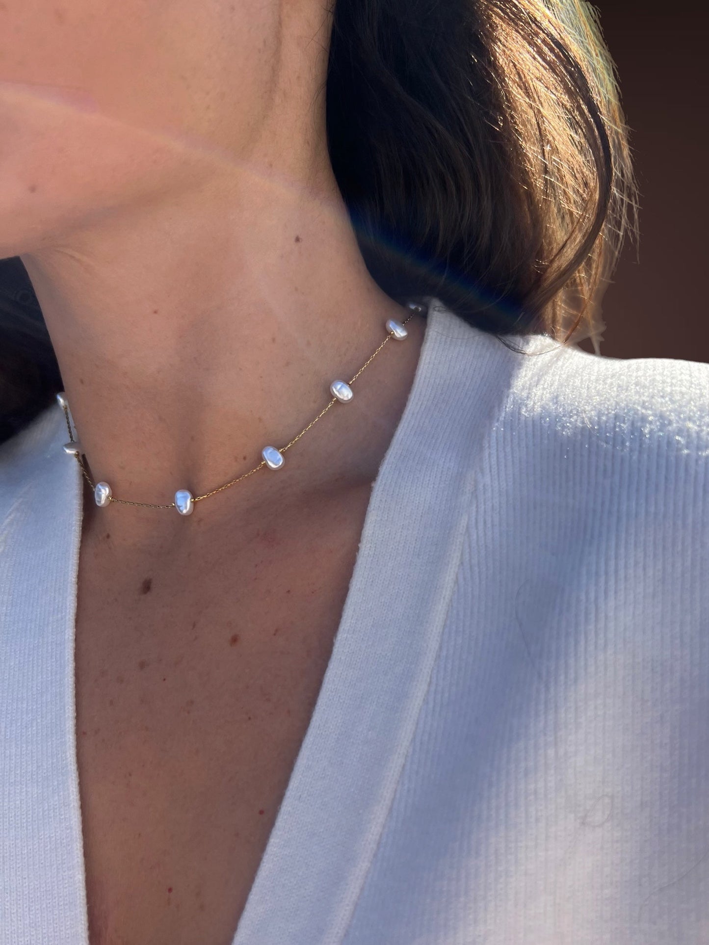 Necklace with pearl-like stones worn by a person in a white outfit.