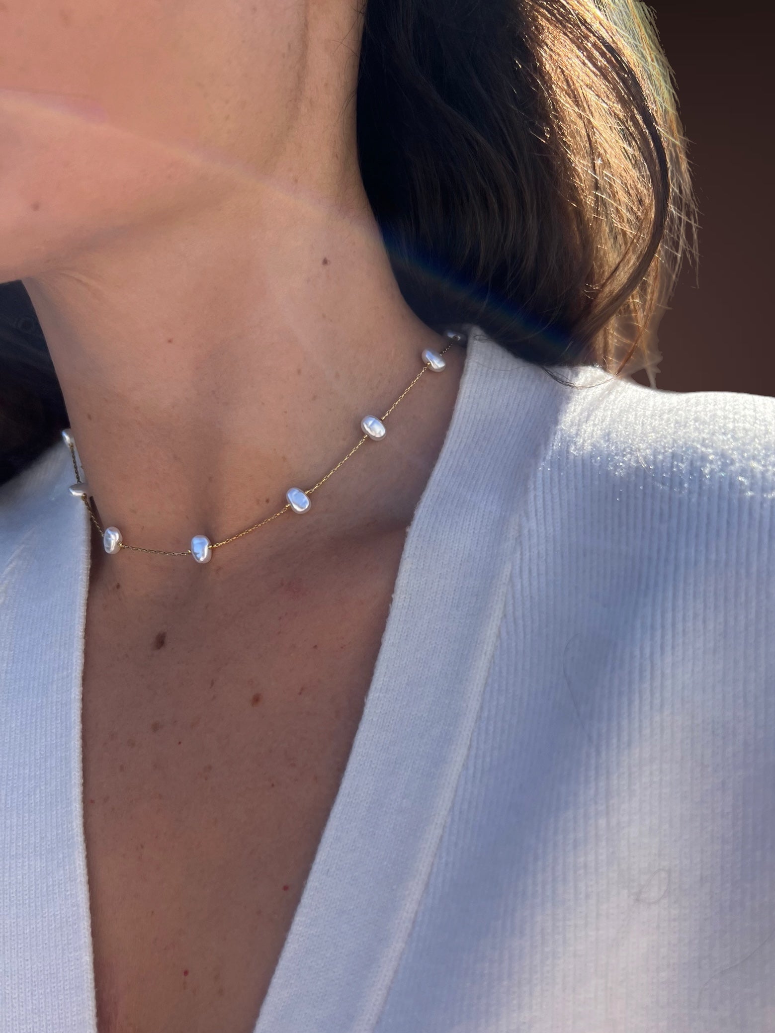 Necklace with pearl-like stones worn by a person in a white outfit.