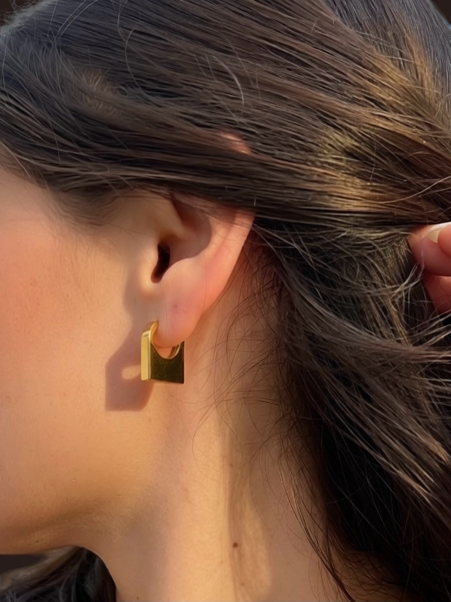 Gold hoop earring worn by a person with brown hair.