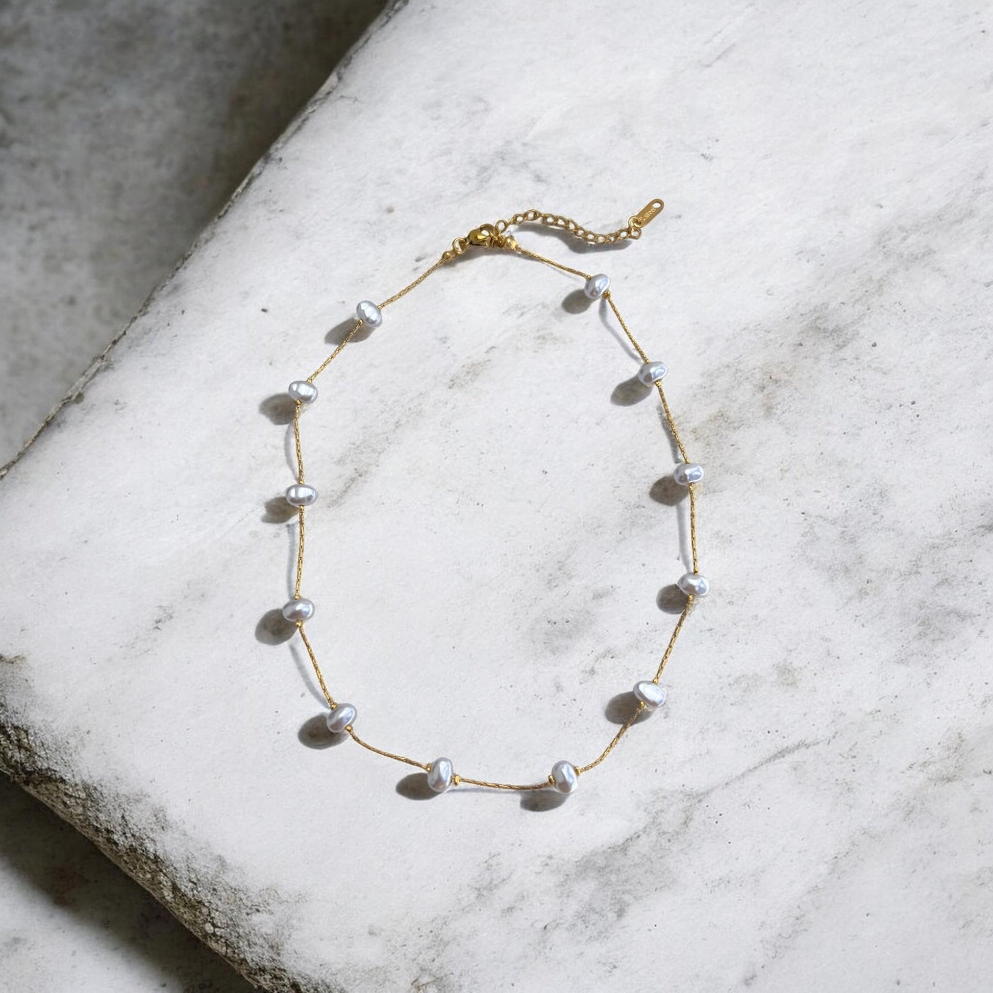 Gold necklace with pearls on a textured white surface