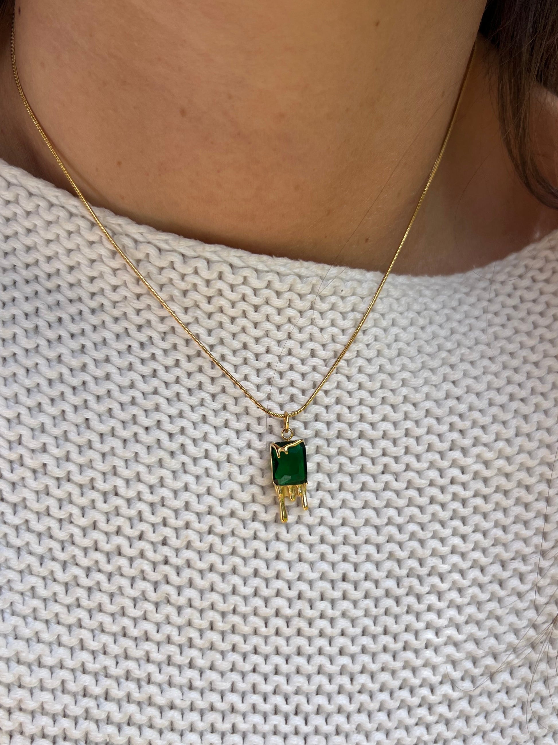 Gold necklace with a green gemstone pendant on a textured white fabric background