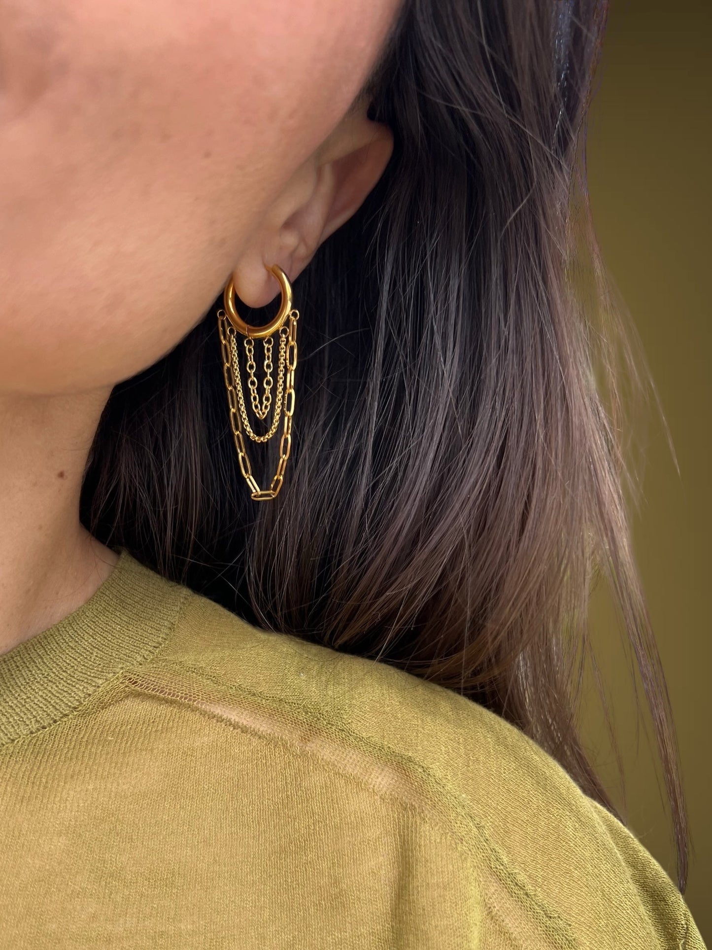 Close-up of a person wearing gold hoop earrings with a blurred background