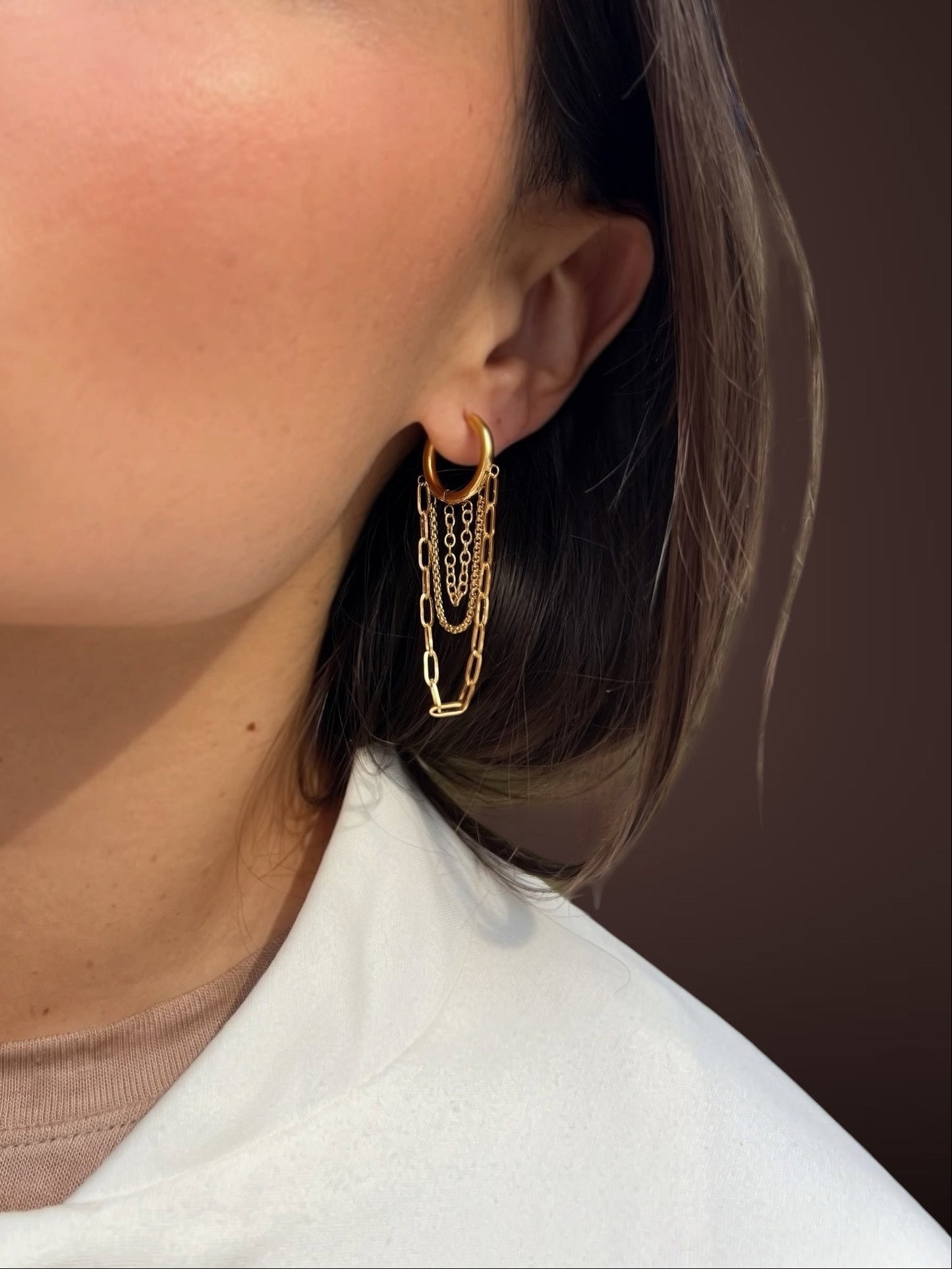 Close-up of a person wearing gold hoop earrings with a neutral background
