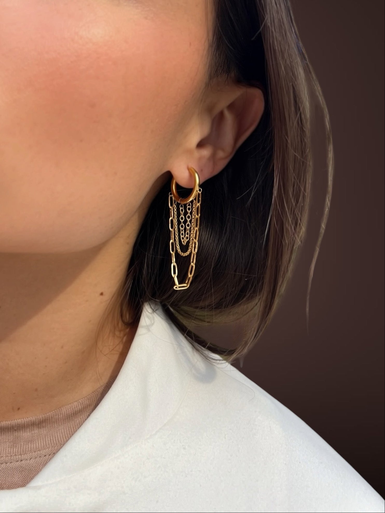 Close-up of a person wearing gold hoop earrings with a neutral background